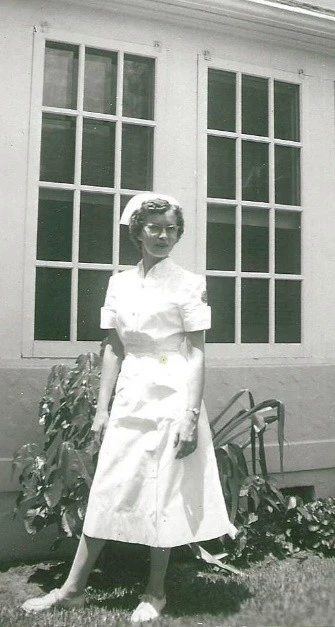 A young Evelyn Thielemann in nurse uniform outside a home. 